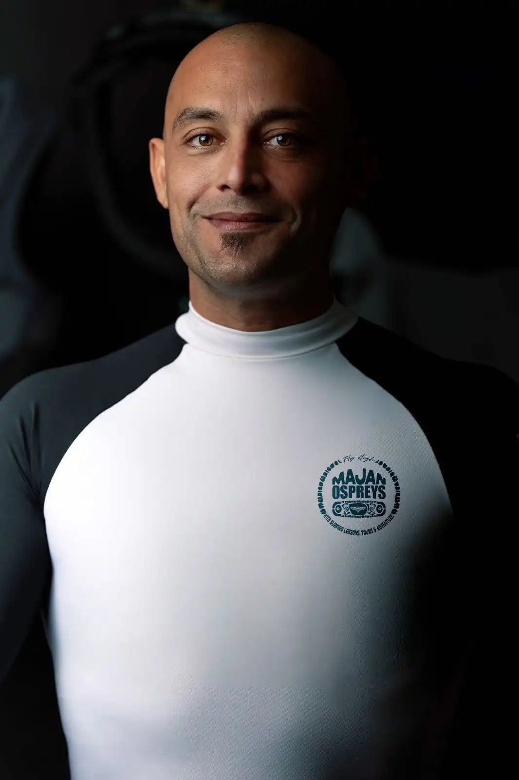 Jamal, founder of Majan Ospreys, wearing a white wetsuit, standing confidently with a beach backdrop